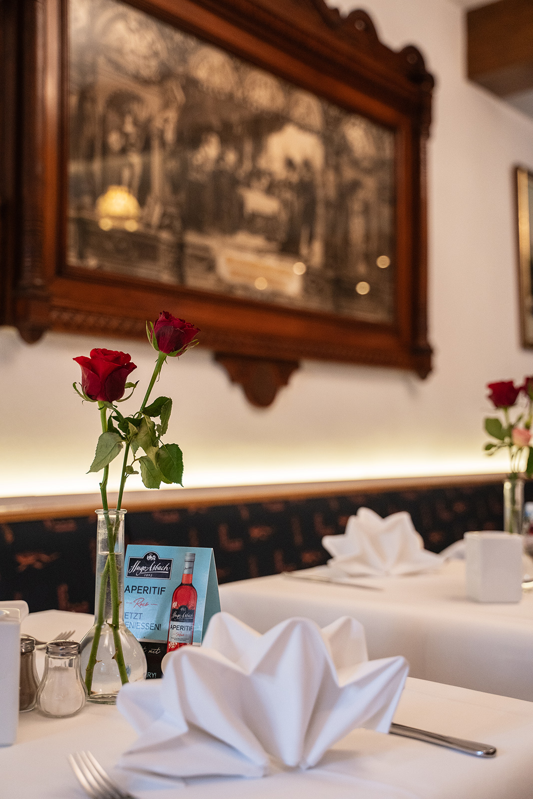 Gedeckter Tisch mit Rosen, Servietten und Werbeaufsteller vor antikem Wandbild
