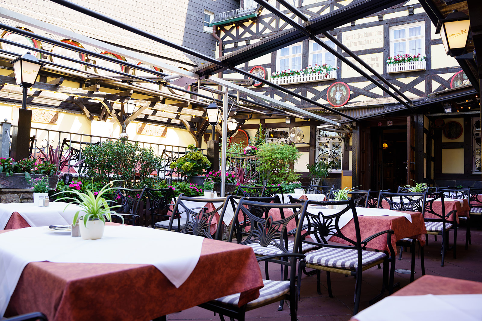 Gedeckte Terrasse mit roten Tischdecken, Pflanzen und Blick auf den Innenhof