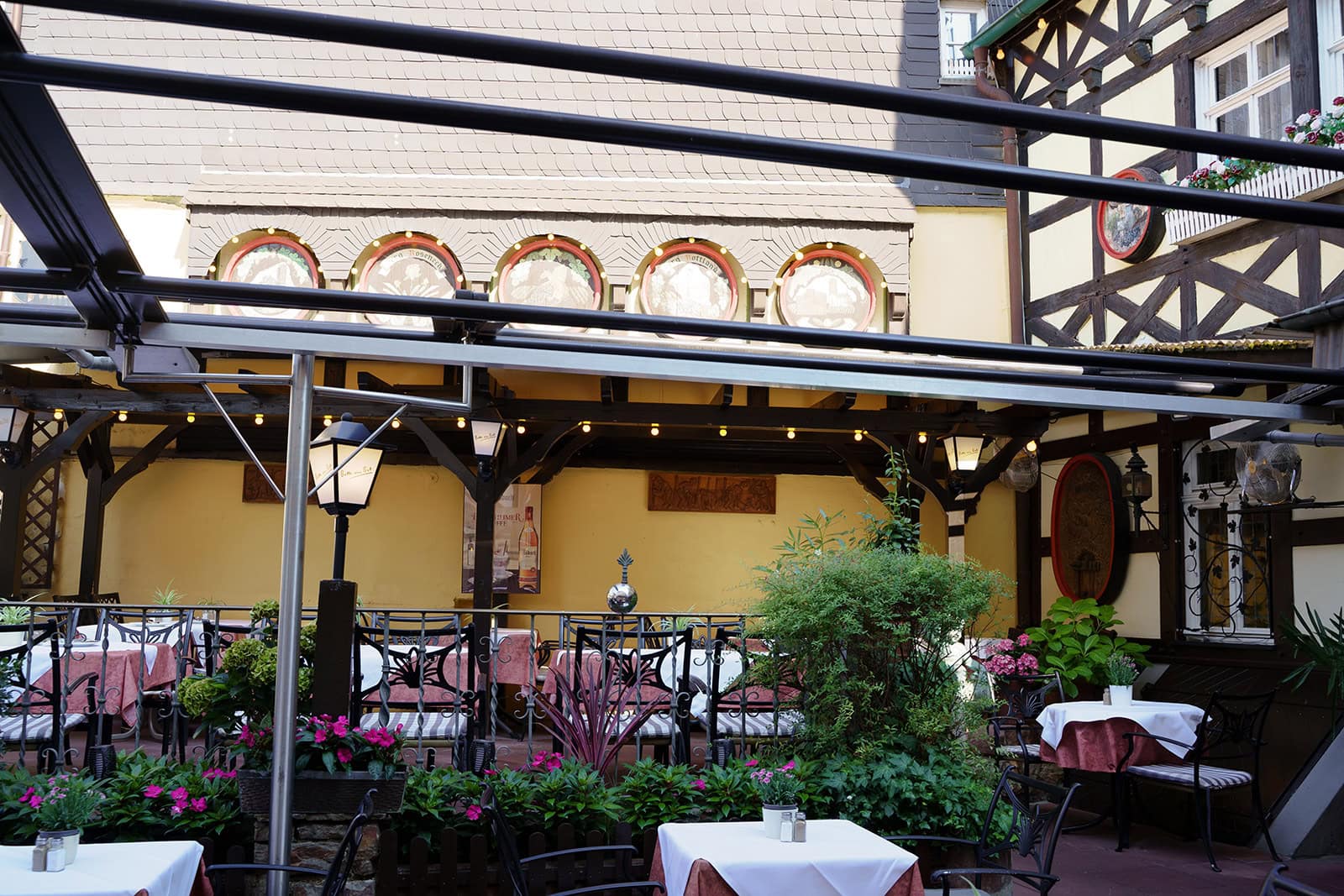 Terrasse mit Geländer, Pflanzen und überdachten Sitzplätzen vor gelber Wand